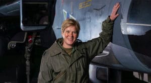 Mandy Hickson standing beside a fighter jet in RAF flying gear, smiling, representing leadership and high-performance decision-making.